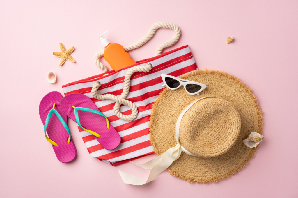 what to pack for beach vacation suitcase luggage Summer travel beach essentials including a striped tote, hat, flip flops, and sunscreen