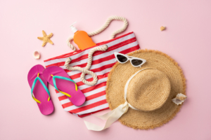 what to pack for beach vacation suitcase luggage Summer travel beach essentials including a striped tote, hat, flip flops, and sunscreen