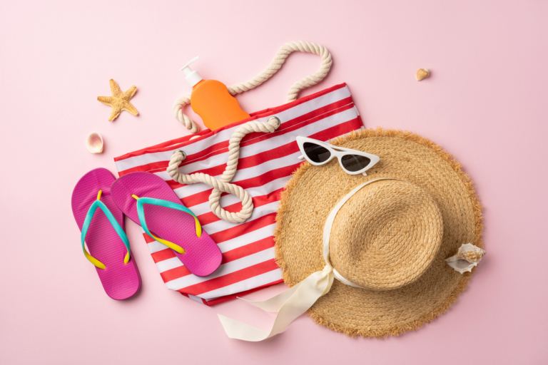 what to pack for beach vacation suitcase luggage Summer travel beach essentials including a striped tote, hat, flip flops, and sunscreen