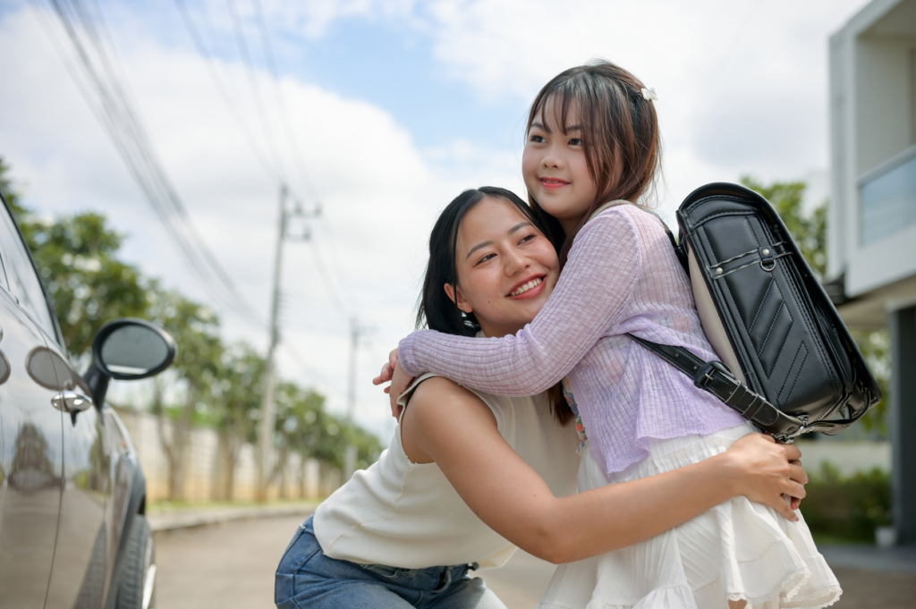 first day of school outfit ideas for moms A caring Asian mom is giving her adorable young daughter a hug in front of the school gate after dropping her off in the morning. back to school, happy family moment