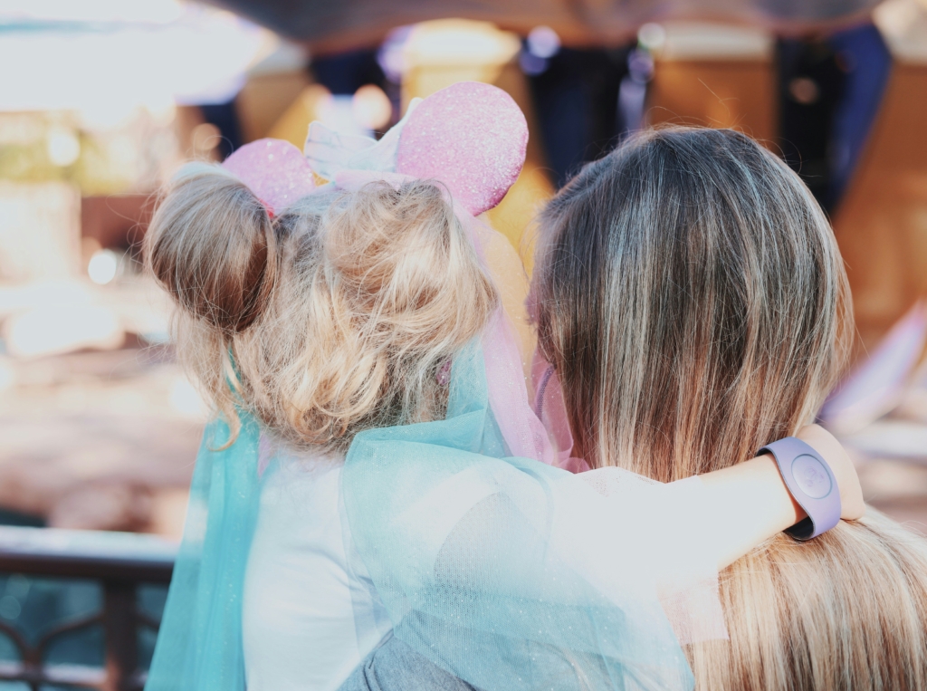 Child with mouse ears hugs adult mom and daughter at disney amusement park family weekend getaway ideas