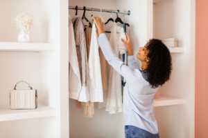 fall capsule wardrobe essentials Woman with curly hair is selecting white blouse from her fashionable wardrobe in a room with chic, minimalist decor and soft lighting