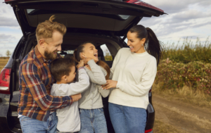 Portrait of happy smiling family of four with two kids boy and girl having fun and hugging standing near the trunk of their car enjoying weekend in nature. Vacation and road trip concept family road trip traveling vacation car ride family weekend getaway ideas
