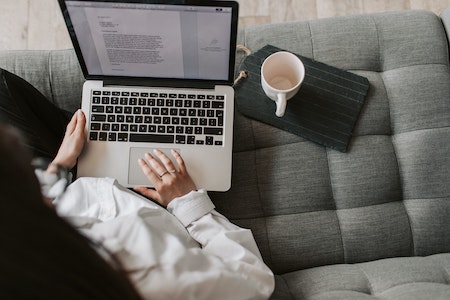 Crop woman using laptop on sofa at home - remote social media jobs