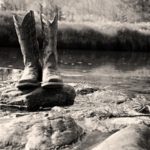 Grayscale Photo of Cowboy Boots on Rock - dresses to wear cowboy boots with