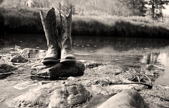 Grayscale Photo of Cowboy Boots on Rock - dresses to wear cowboy boots with