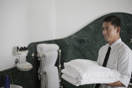 Hotel worker with clean towels in bathroom - housekeeper jobs
