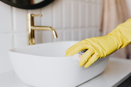 Person in glove cleaning bathroom sink - housekeeper jobs