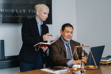 Ethnic male lawyer showing document on laptop to young female colleague - remote paralegal jobs