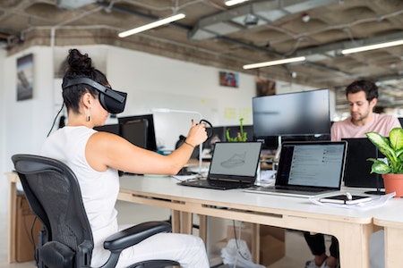 Woman at computer with VR headset - tech sales jobs