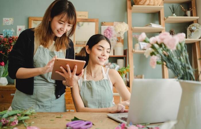 Happy women working on gadgets in floral store - creative jobs near me