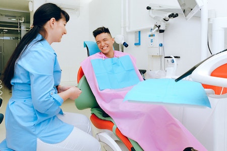 Cheerful ethnic male patient sitting in dental chair in clinic - hire dental assistant