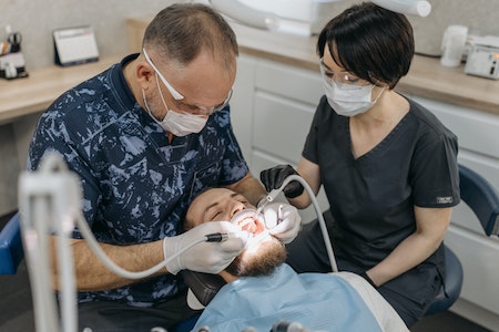 A Dentist and His Dental Assistant Working on a Patient - hire dental assistant