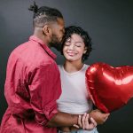Man Kissing His Woman While Holding a Red Heart Shaped Balloon - best Valentine's Day jewelry deals