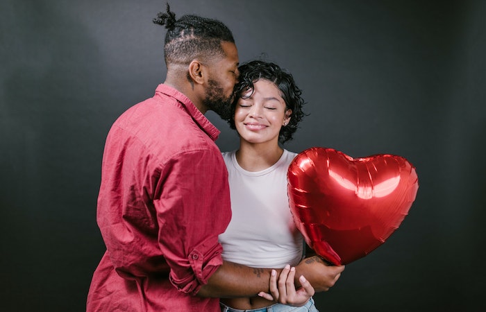 Man Kissing His Woman While Holding a Red Heart Shaped Balloon - best Valentine's Day jewelry deals