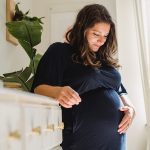 Smiling pregnant woman caressing tummy in house room - prenatal vitamins to get pregnant
