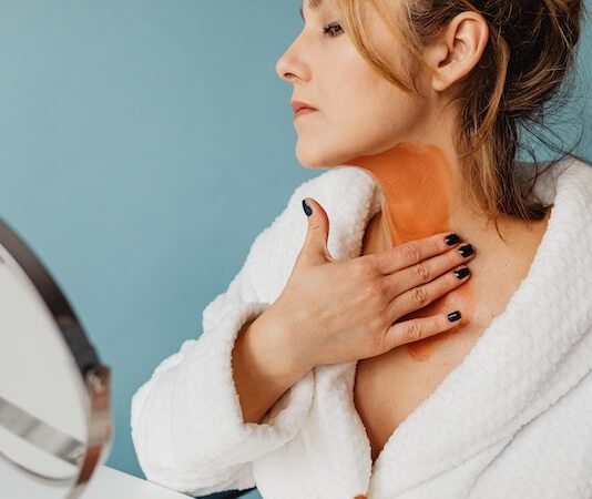 Photo of a Woman Applying Brown Cream to Her Neck - best neck firming cream