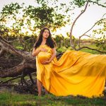 Pregnant Woman in Yellow Gown Posing in front of Fallen Tree - maternity photoshoot ideas