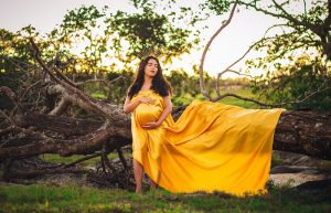 Pregnant Woman in Yellow Gown Posing in front of Fallen Tree - maternity photoshoot ideas