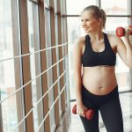 Cheerful pregnant woman doing exercises with dumbbells - maternity workout clothes