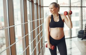 Cheerful pregnant woman doing exercises with dumbbells - maternity workout clothes