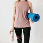 Crop sportswoman carrying sport mat and bottle of water before exercising - barre vs pilates