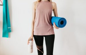 Crop sportswoman carrying sport mat and bottle of water before exercising - barre vs pilates