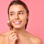 Beautiful woman doing massage for face lift and anti wrinkle using microneedling mesotherapy and serum isolated on pink background. Facial skin care, cosmetology, beauty concept. ice rolling