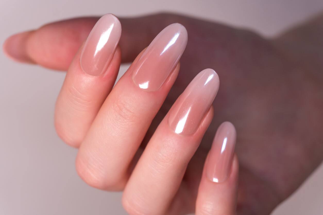 chrome nails winter nail color trends Detailed studio shot highlighting professional nail art. The nails are long and shaped in a soft oval, featuring a delicate nude-to-pink ombre gradient and a highly reflective, glossy, iridescent chrome top coat. Excellent for beauty salons, cosmetics advertising, or nail care tutorials and blogs.