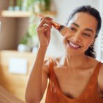 woman doing her makeup spring break beauty routine Beautiful girl applying makeup using powder brush before going to work. Healthy latin woman looking in the mirror and applying cosmetic with a big brush. Young woman looking in the mirror and applying foundation or blusher on her face.